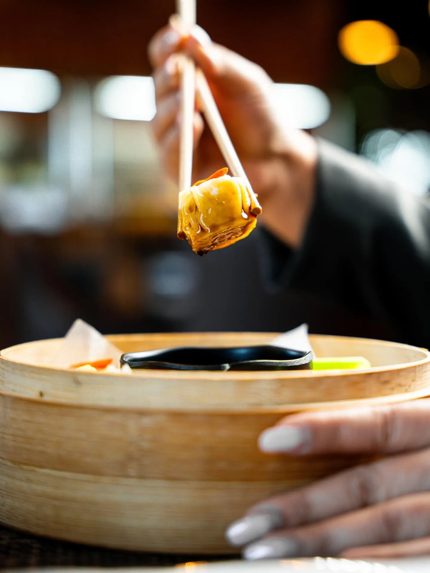 A dumpling held up on chopsticks in shallow focus, a restaurant interior behind