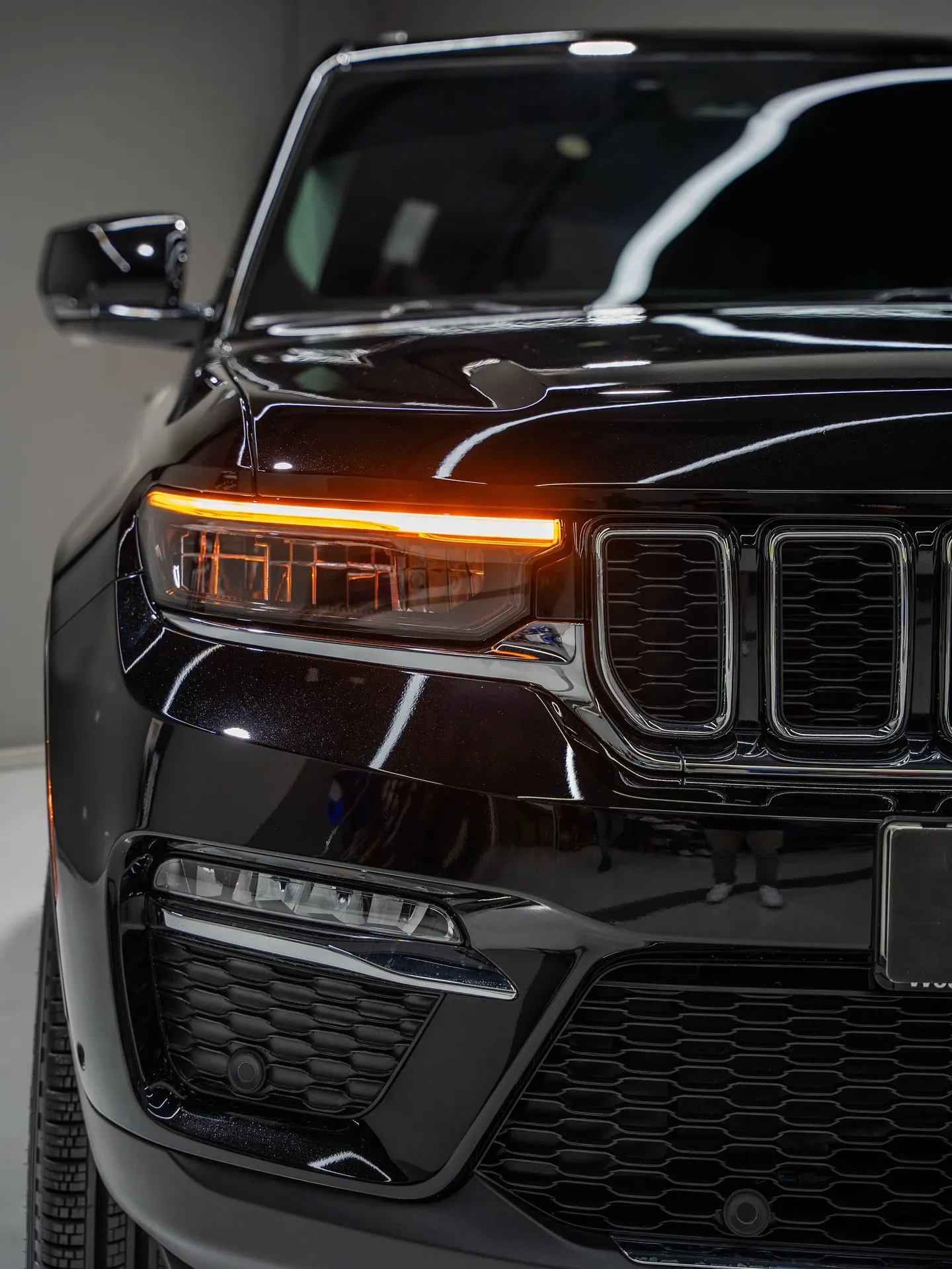 The front grille and lit headlamp of a black SUV in a showroom