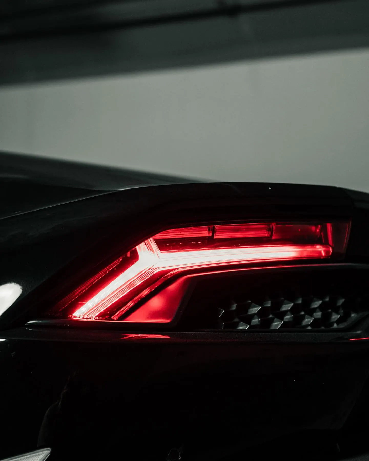 The illuminated red tail light of a dark sports car, the rest of the body in shadow