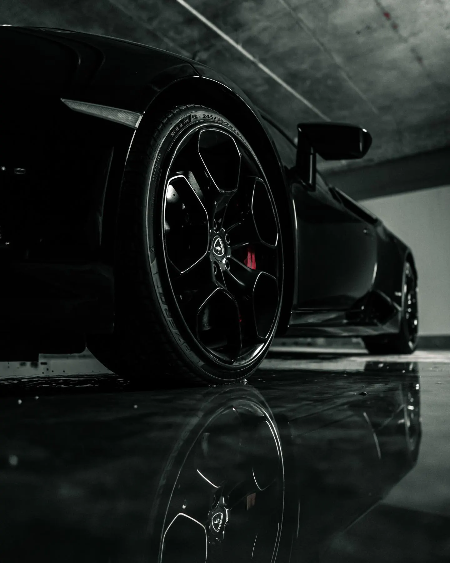 Close detail of the alloy wheel and arch of a dark sports car against a black background