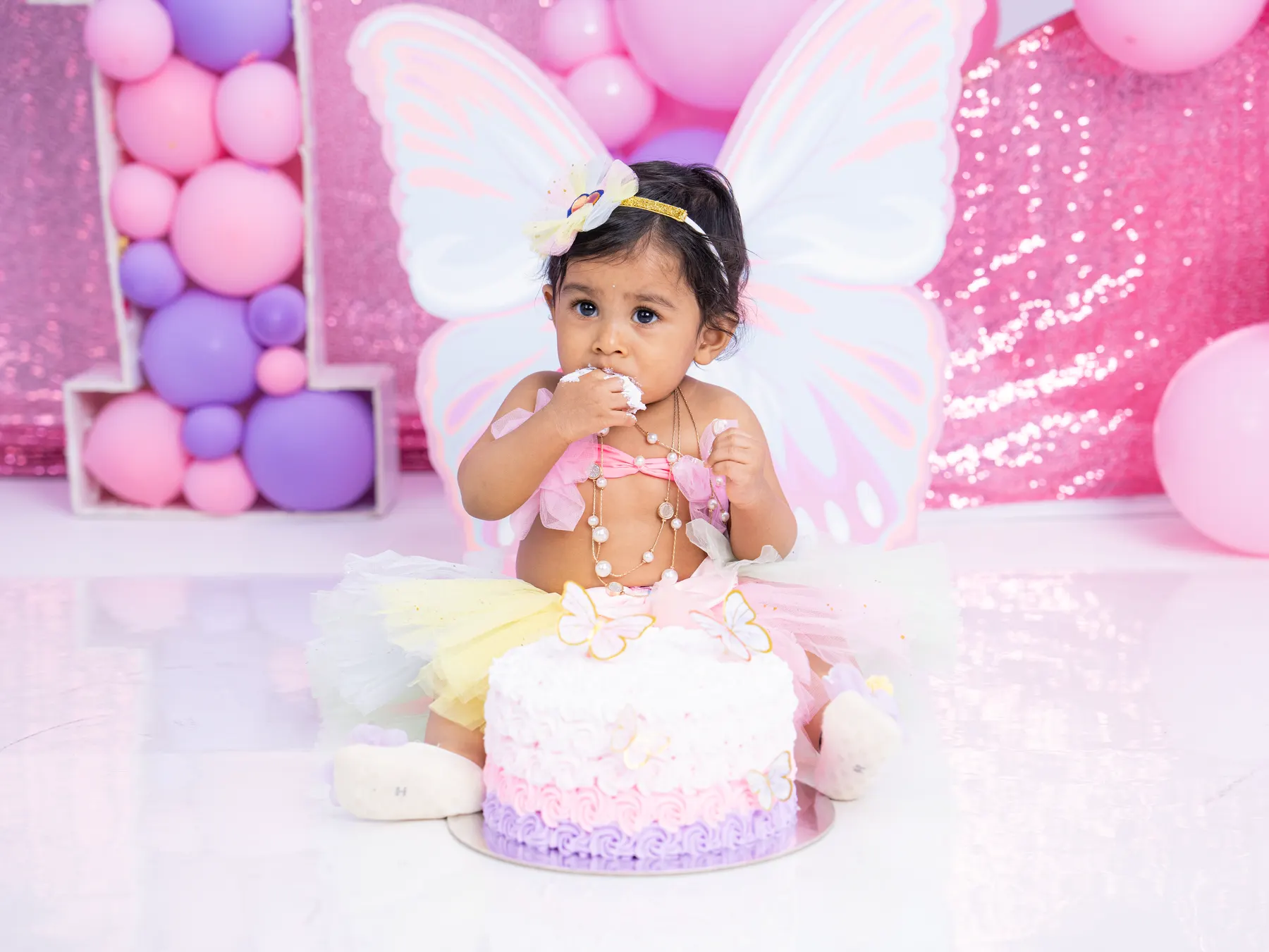 Child in fairy wings at a pink first-birthday party setup