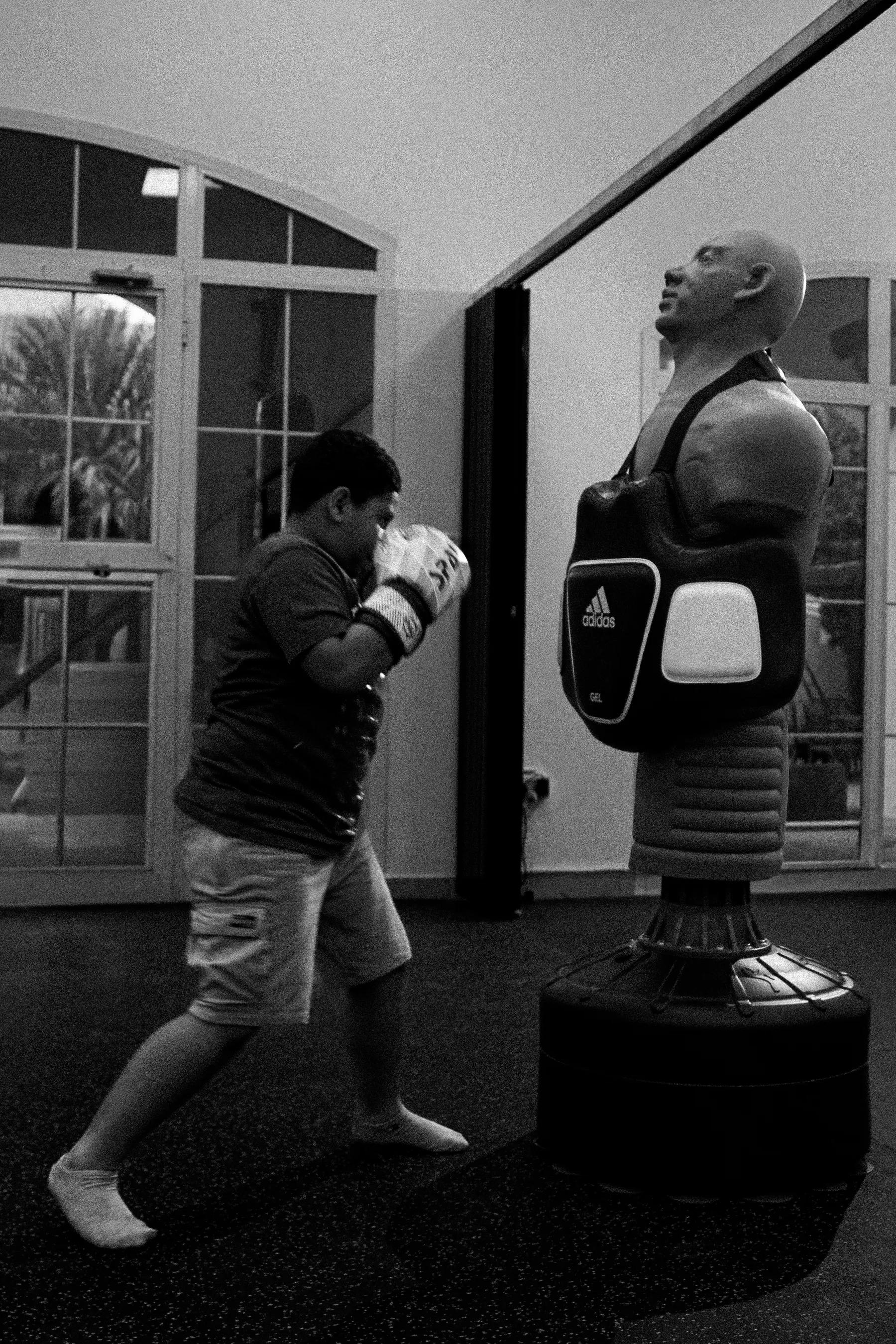 Black and white photograph of a young boxer training on a free-standing punch bag