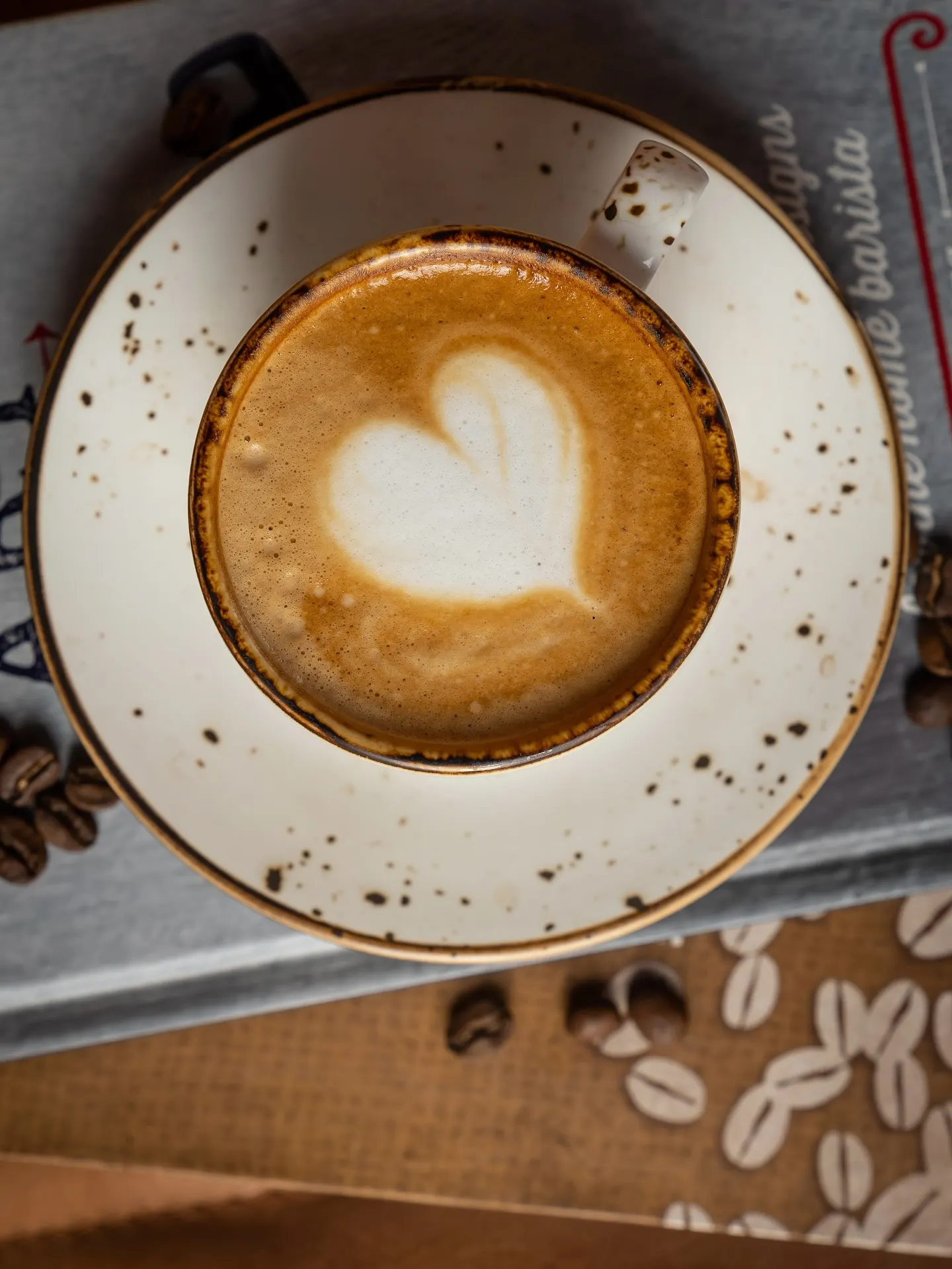 A flat white photographed from above, a heart poured into the crema of a speckled ceramic cup