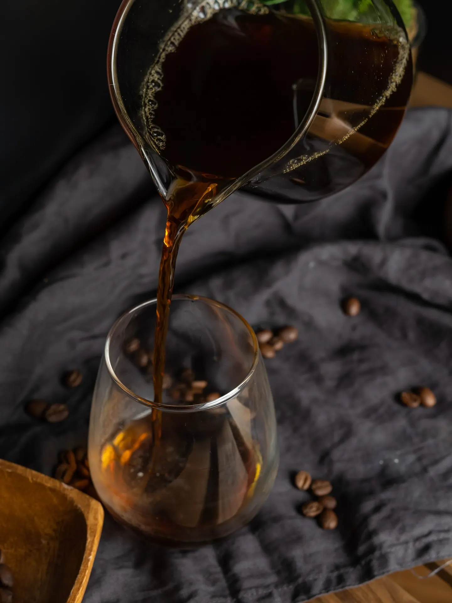 Coffee being poured from a jug into a stemmed glass against a dark background