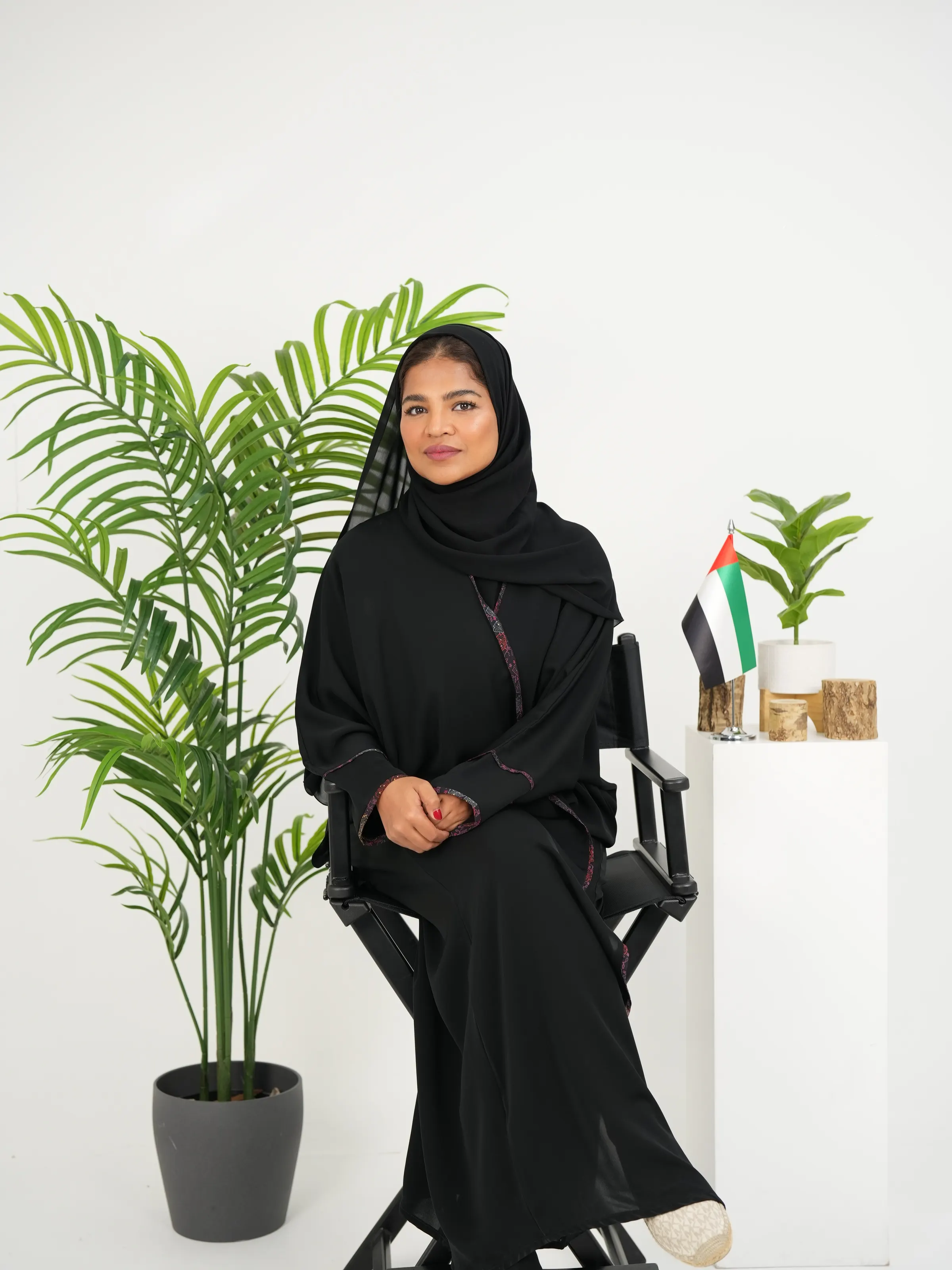 Seated corporate portrait of a woman in an abaya against a white backdrop