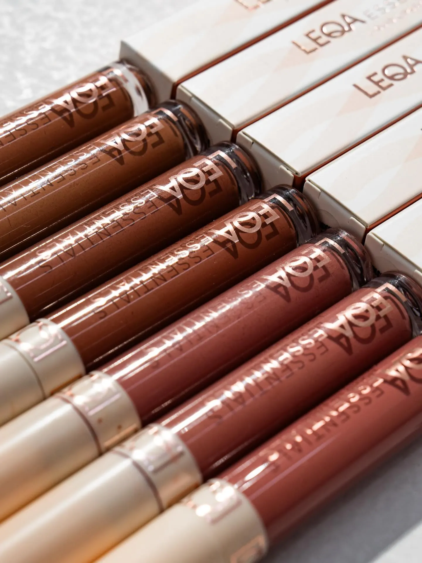 Six lip gloss tubes in graduated shades laid in a row on a pale surface