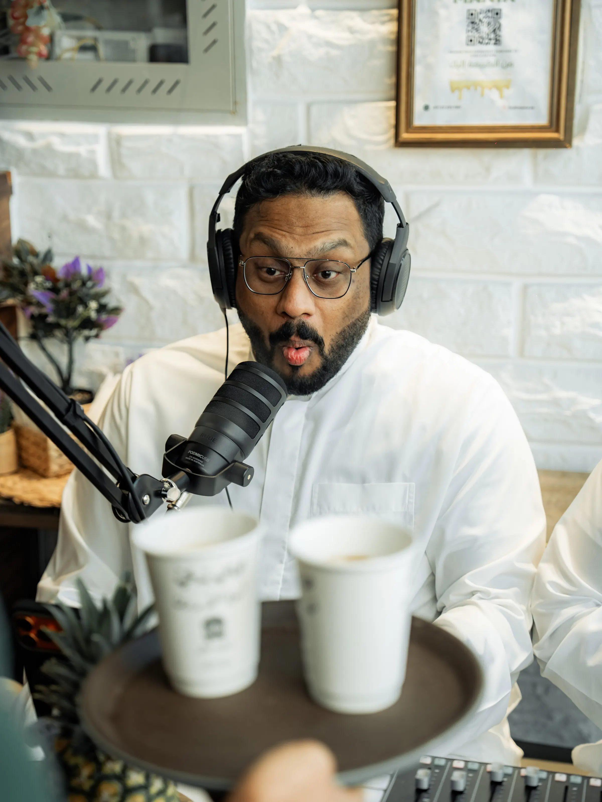 Podcast host at a microphone with coffee cups on a tray