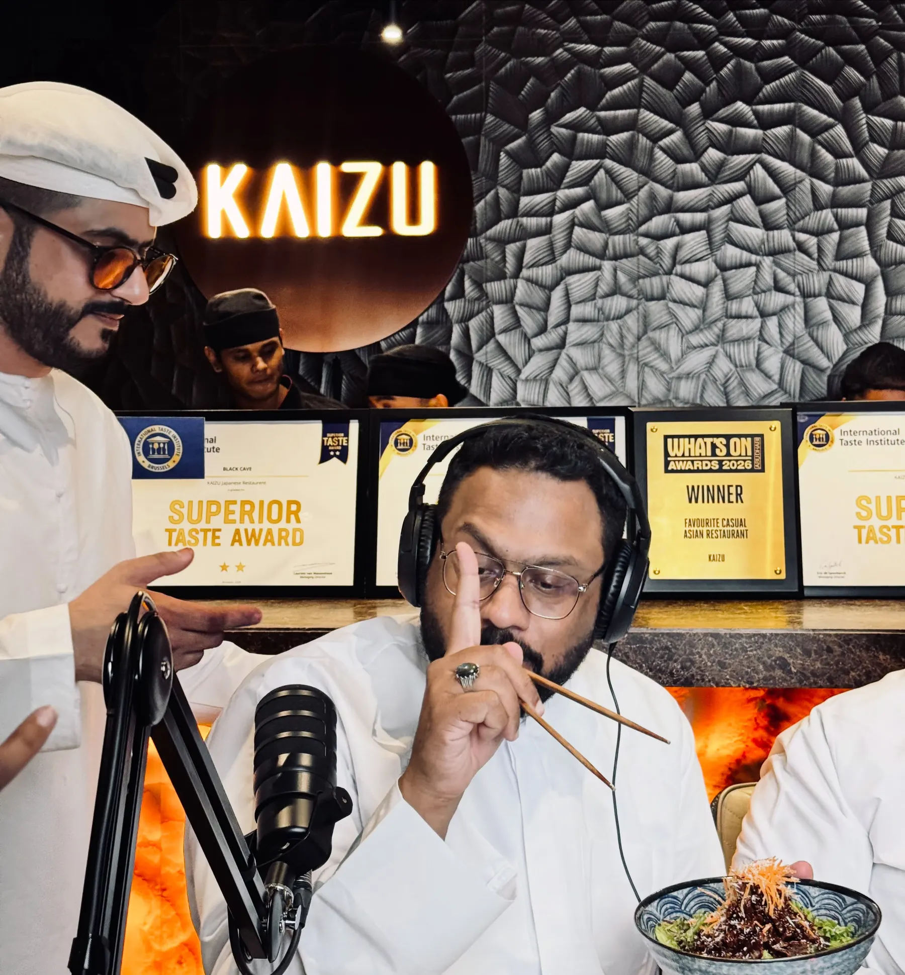 Two hosts eating noodles at a restaurant podcast set