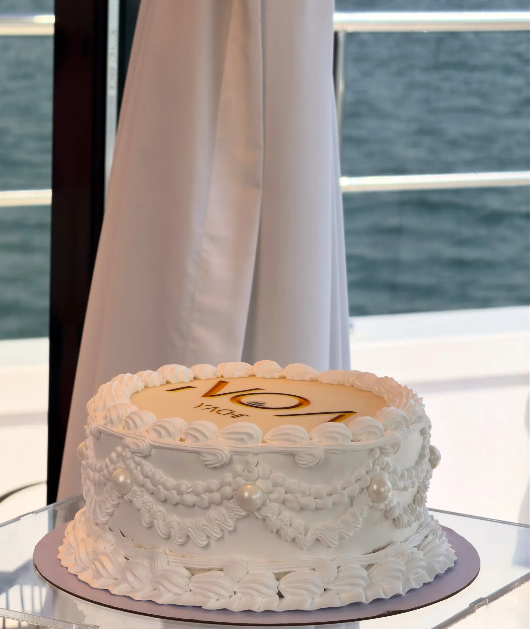 A plain white celebration cake on a stand aboard a yacht