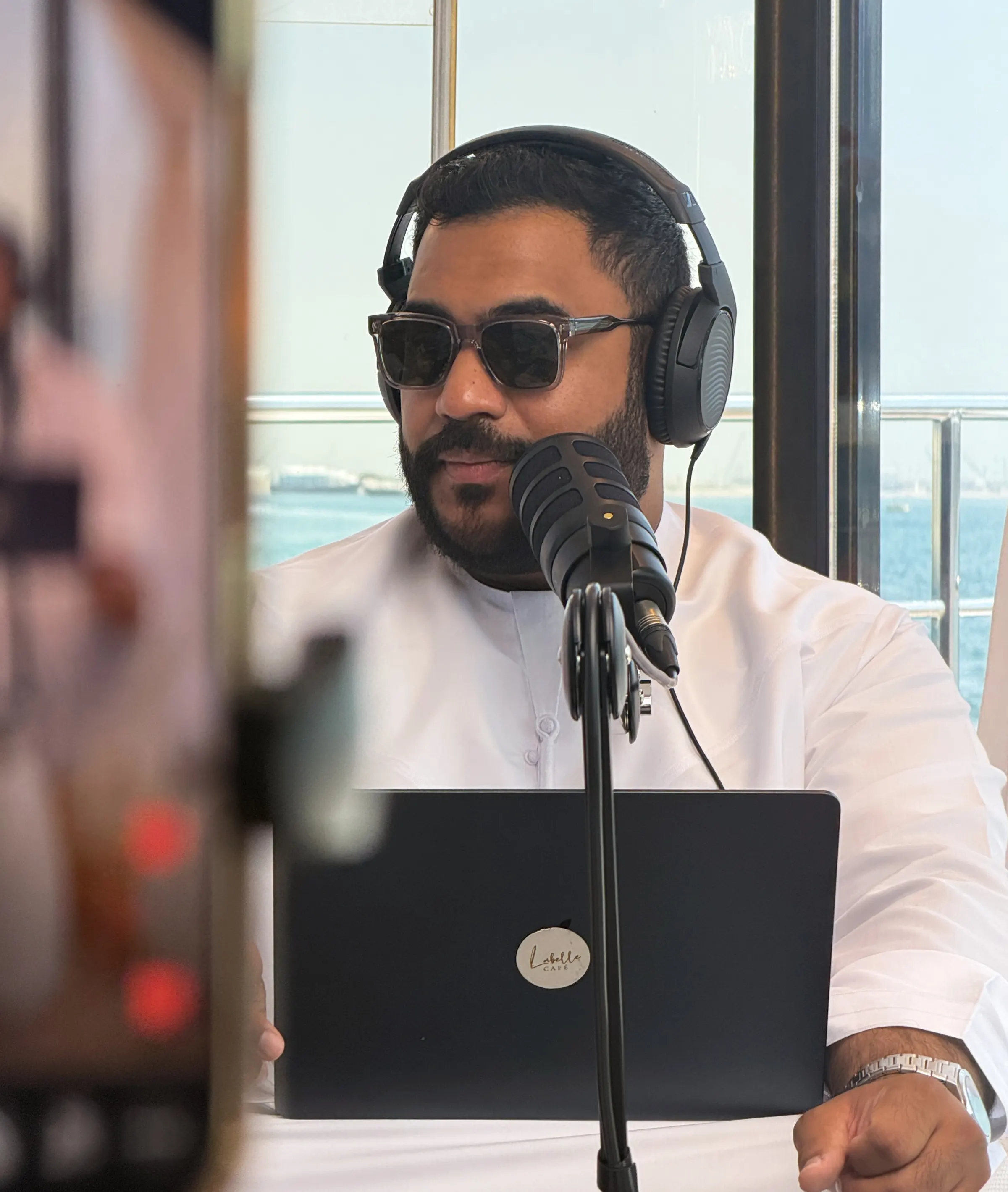 Podcast host in sunglasses and headphones at a microphone on a yacht