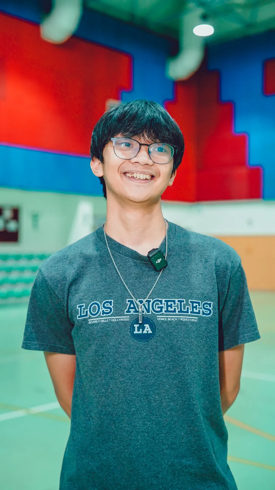 Andrew Salvador smiling in glasses and a grey Los Angeles T-shirt in a sports hall