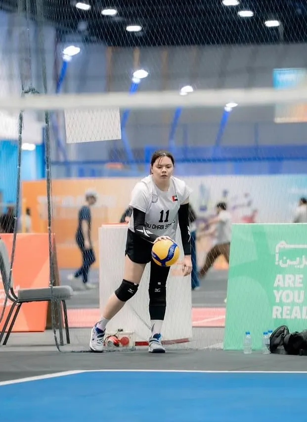 An Abu Dhabi Spikers player in a white number 11 jersey and knee pads, holding a volleyball at the net on an indoor court