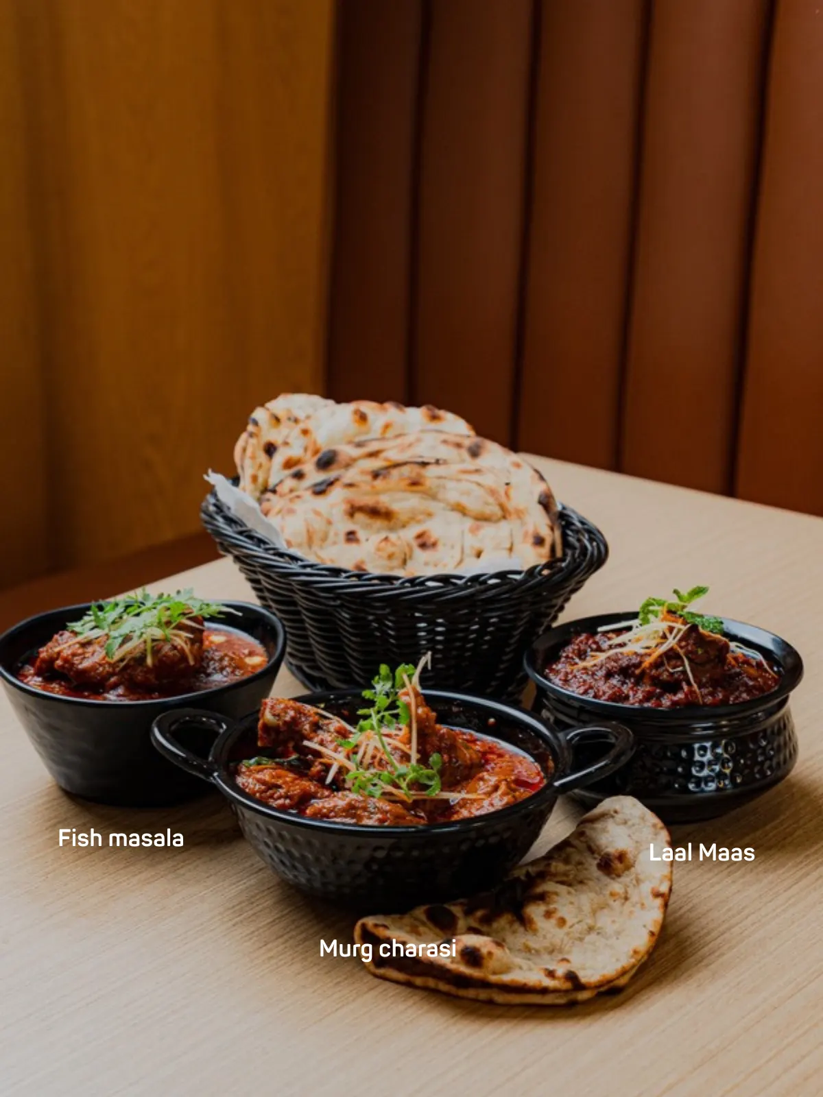 Indian restaurant spread of curries and breads served in black bowls