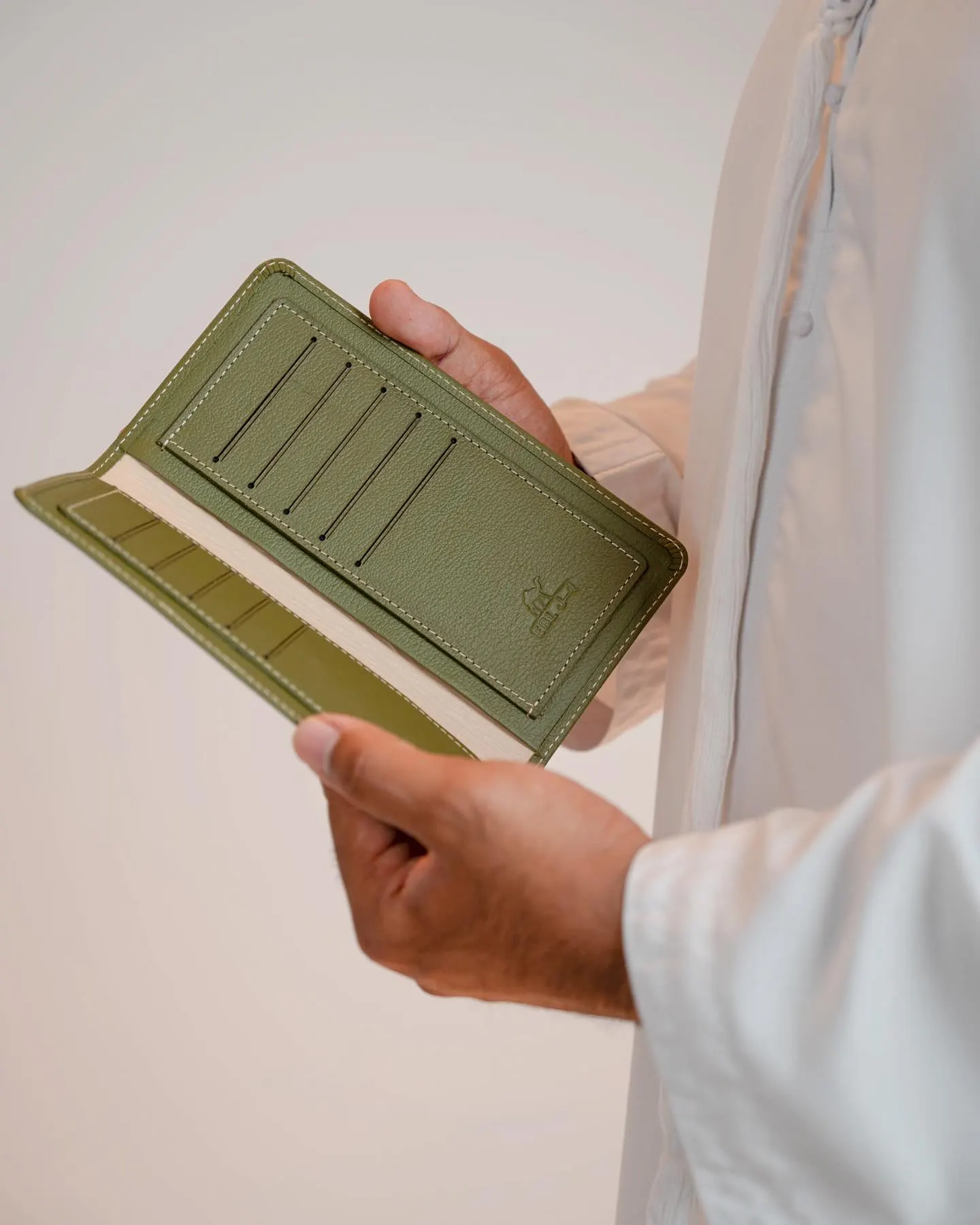 A green leather wallet held open in one hand against a pale background