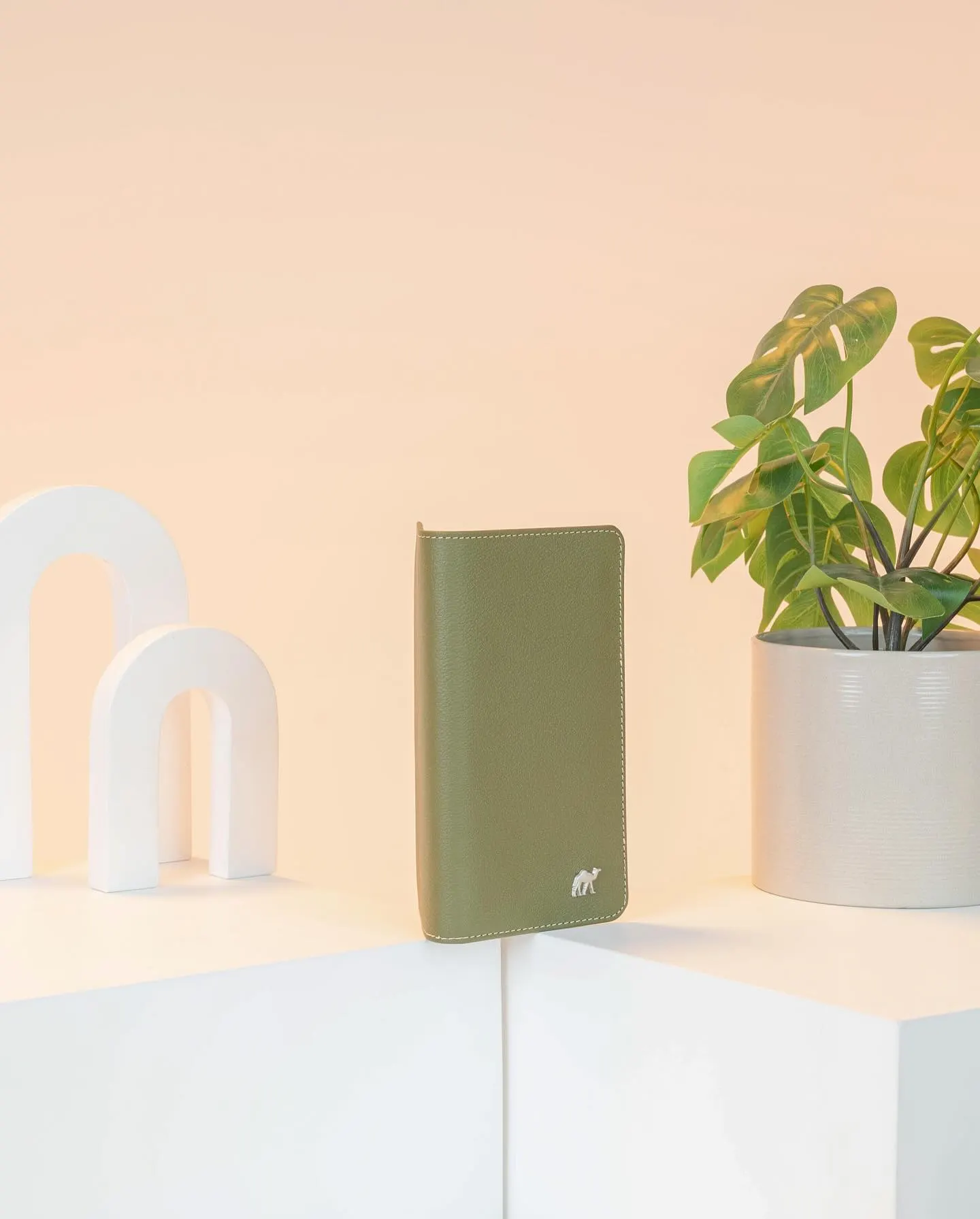 A green leather wallet standing on a pale plinth between two potted plants