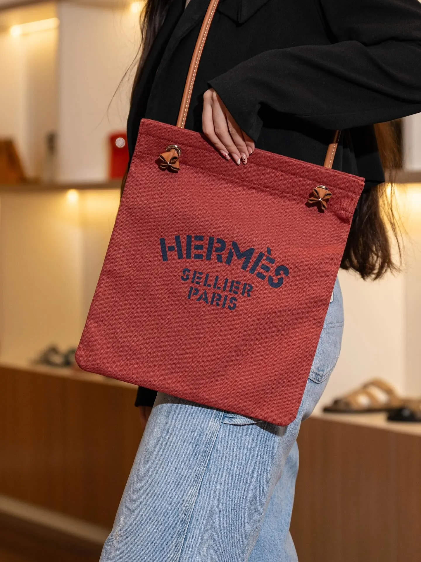 A person in black carrying a red leather tote bag over one shoulder