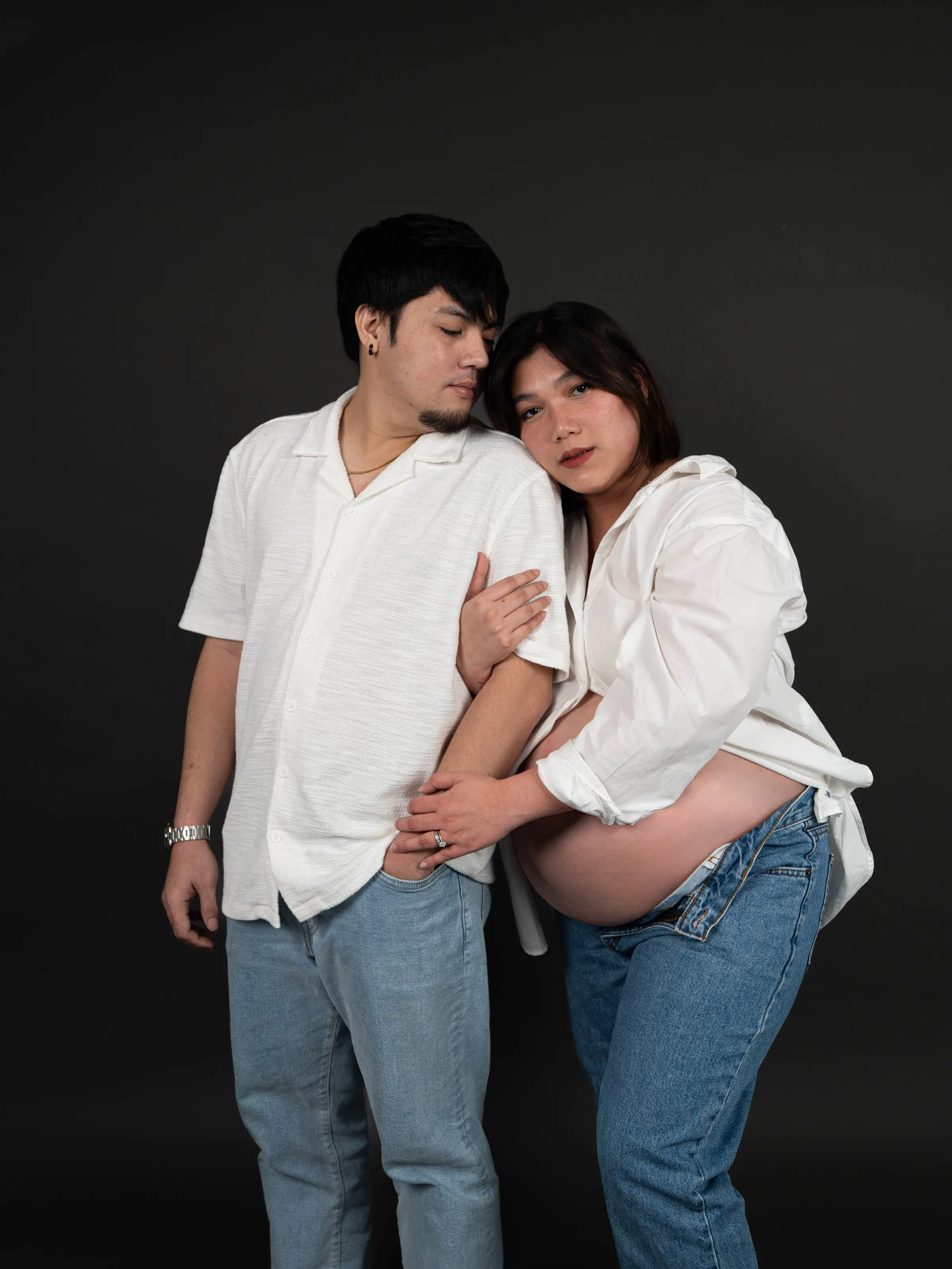 Maternity couple portrait against a dark studio backdrop