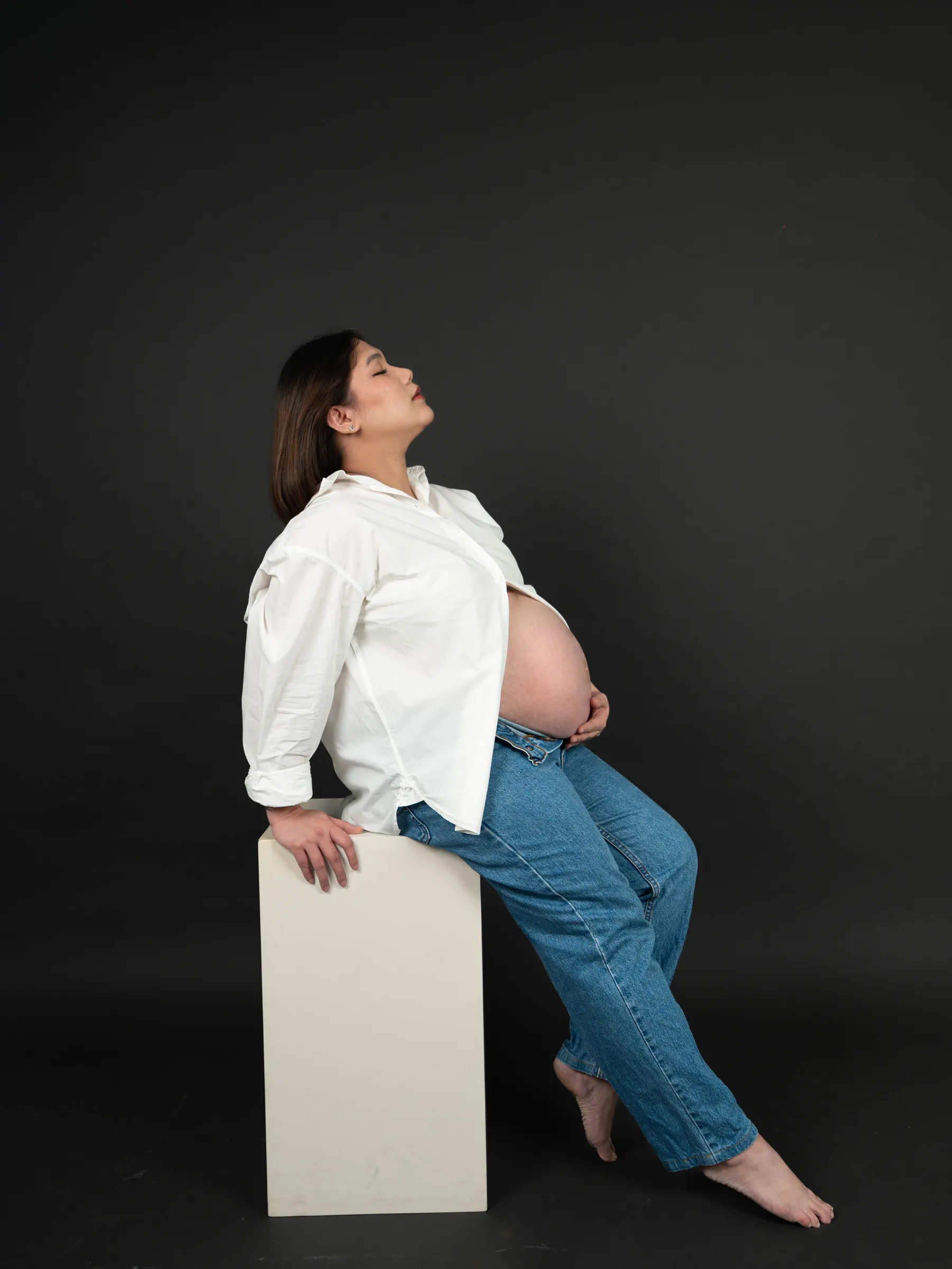 Expectant mother seated on a plinth against a dark studio backdrop