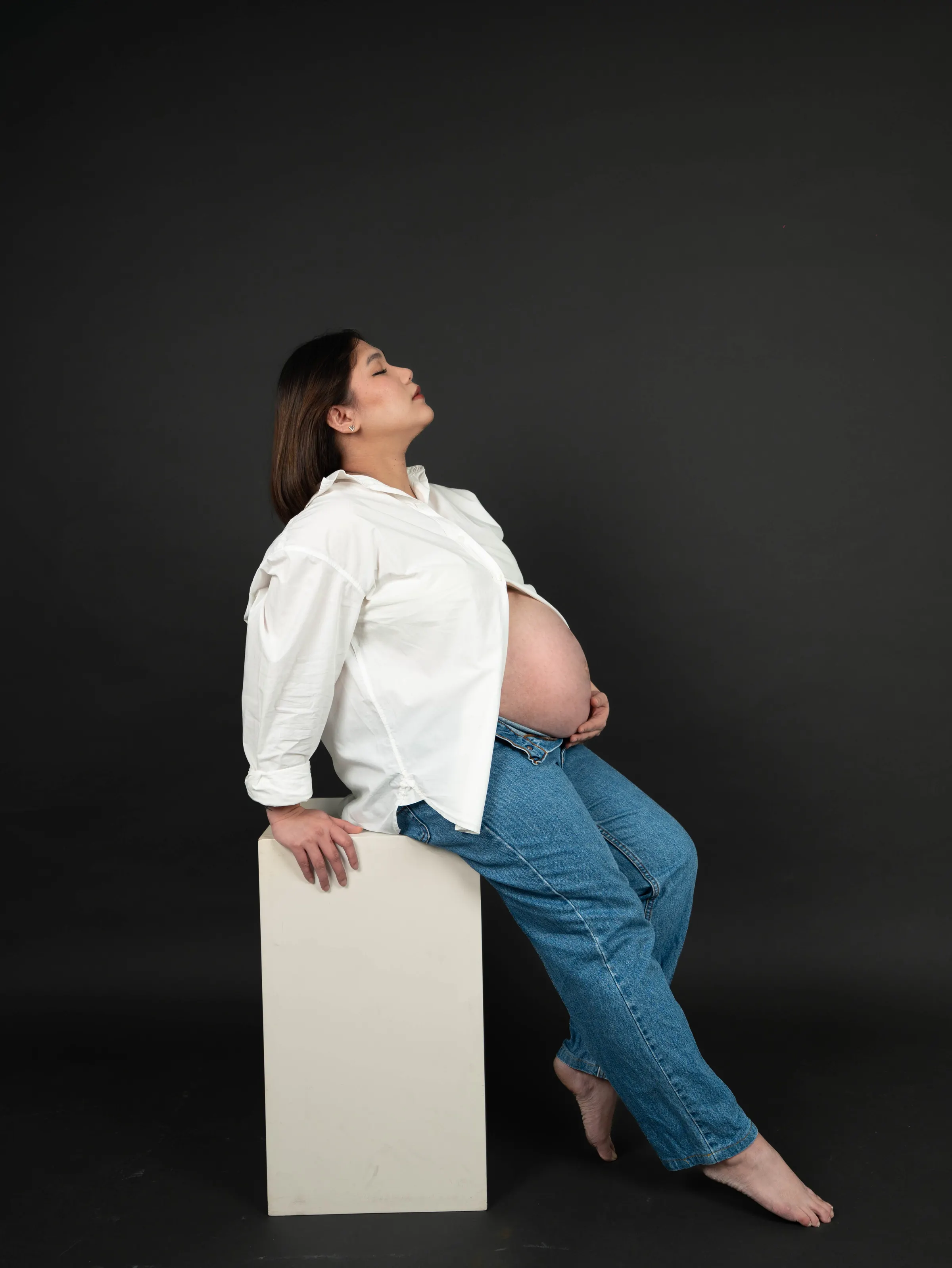 Expectant mother seated on a plinth against a dark studio backdrop