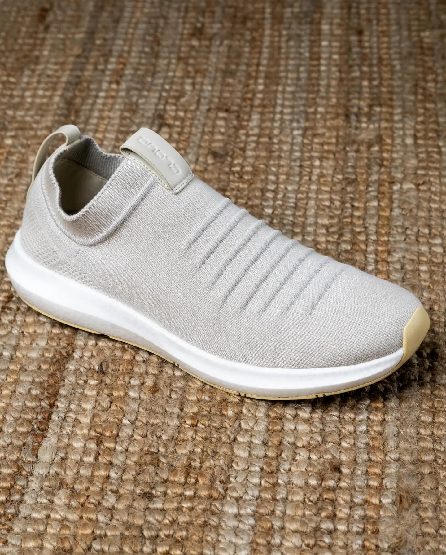 One white knitted slip-on shoe photographed on woven matting