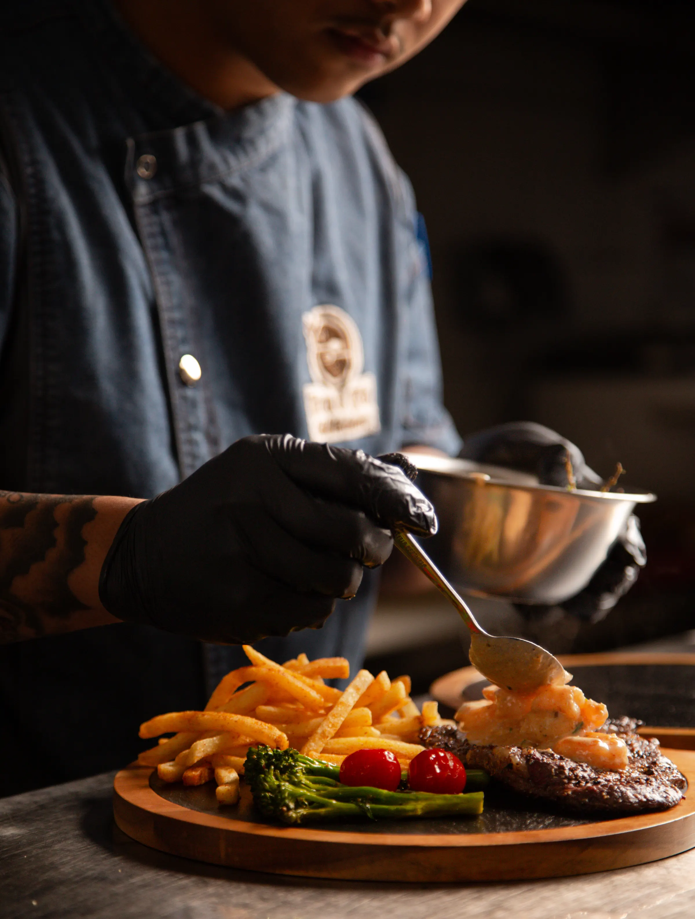 Chef spooning sauce over a plated steak and fries on a wooden board