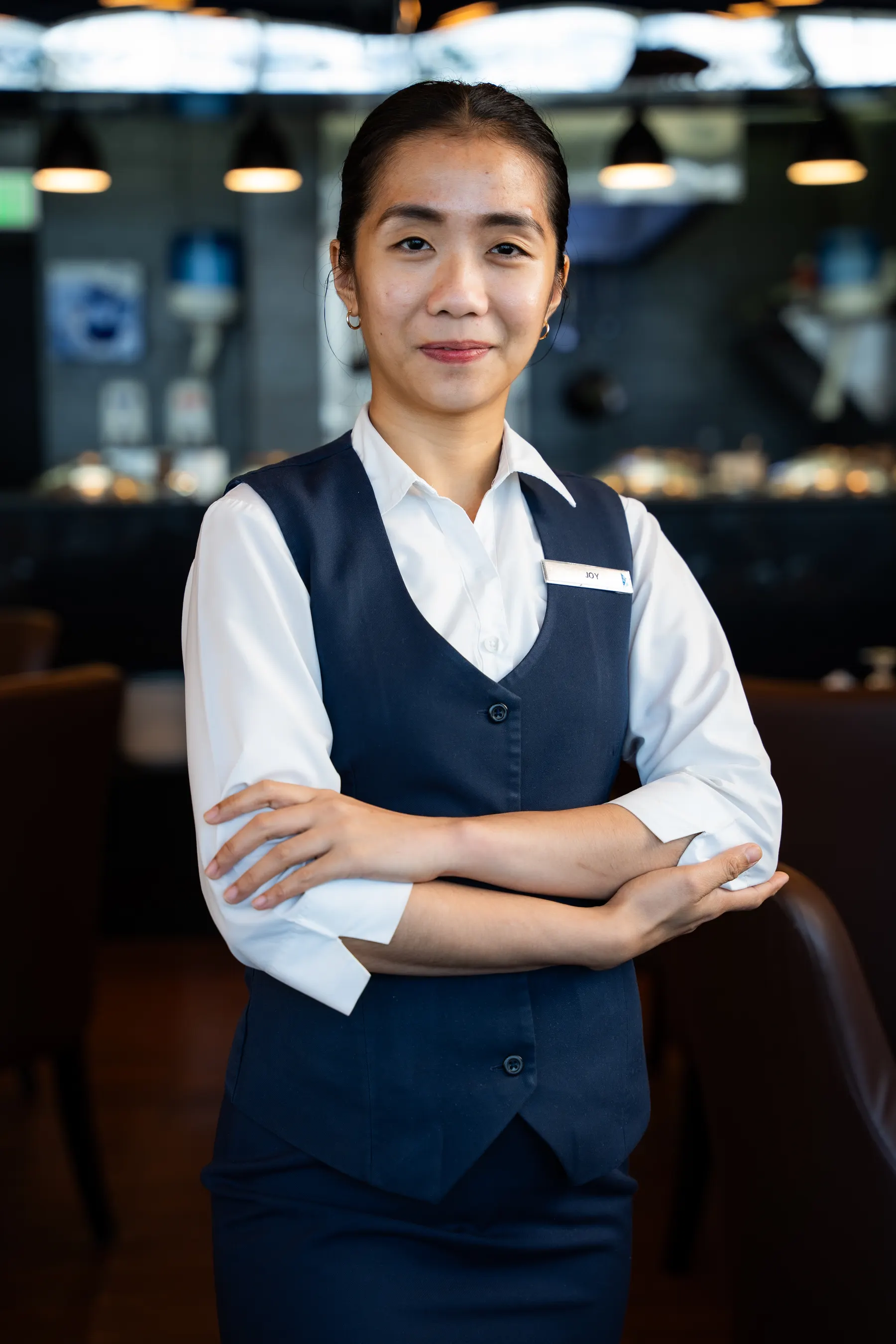 Restaurant staff member standing with arms folded in a dining room