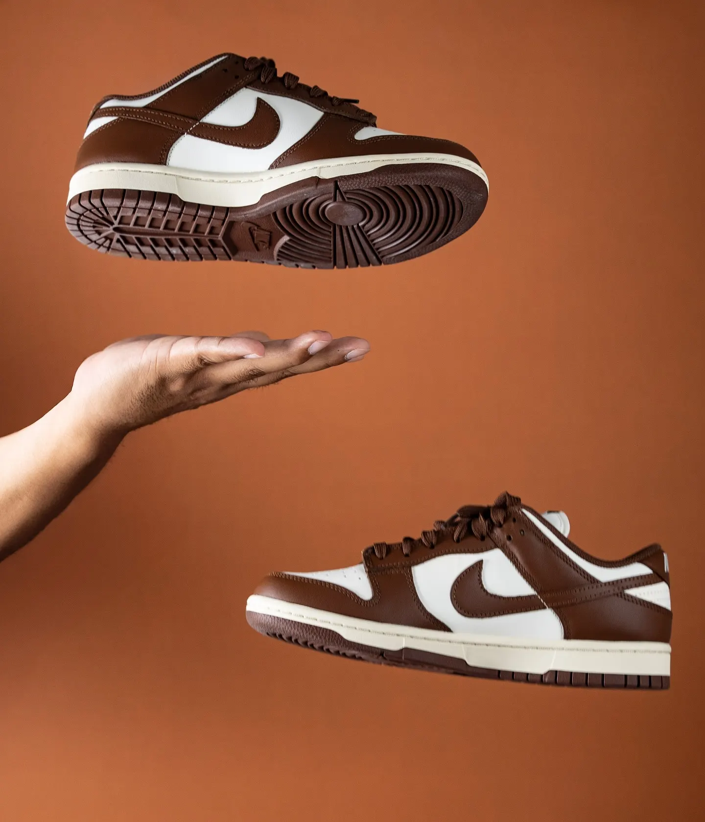 A white and brown sneaker held above an open hand against an orange background