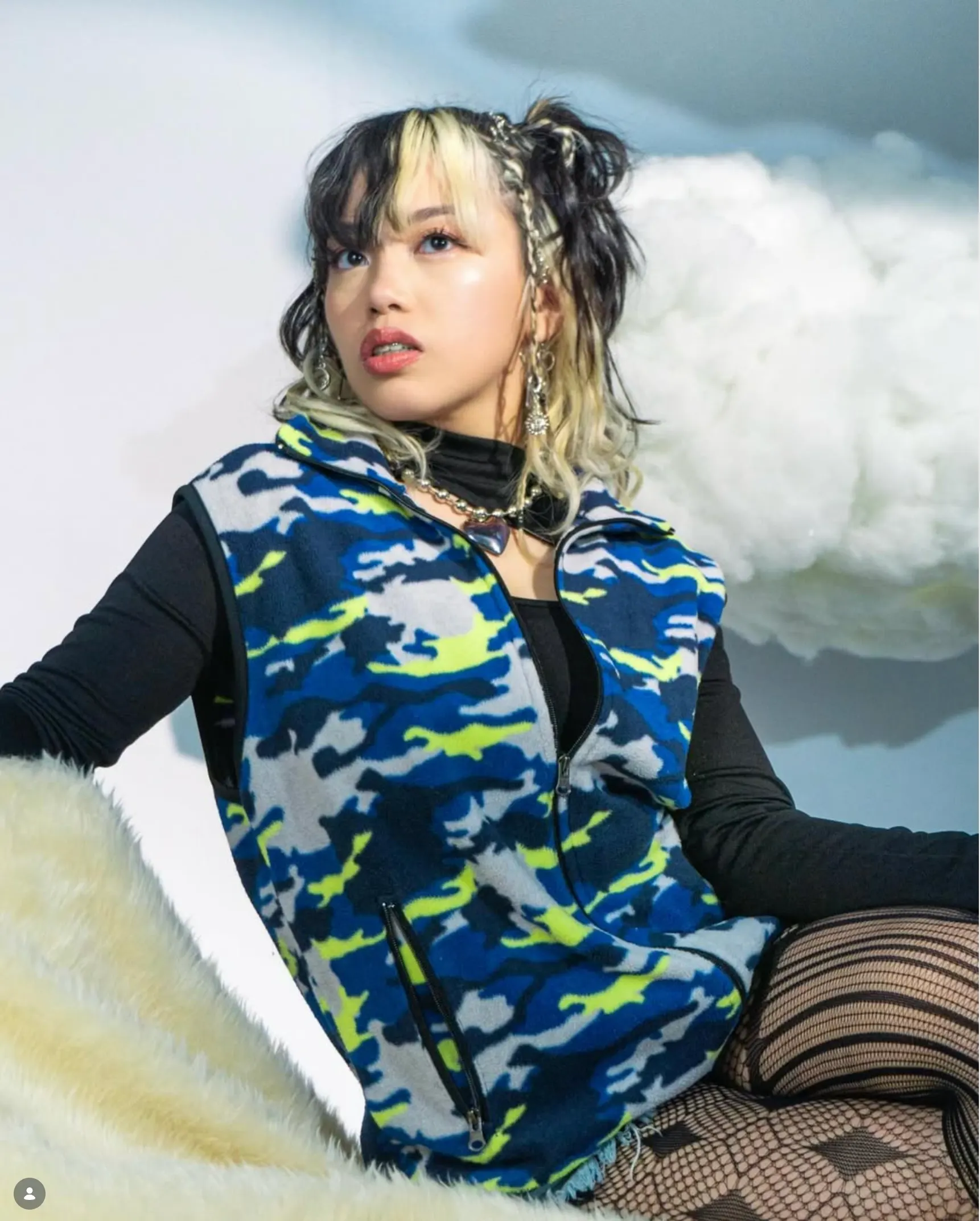 A studio portrait of a person in patterned outerwear against a painted cloud backdrop
