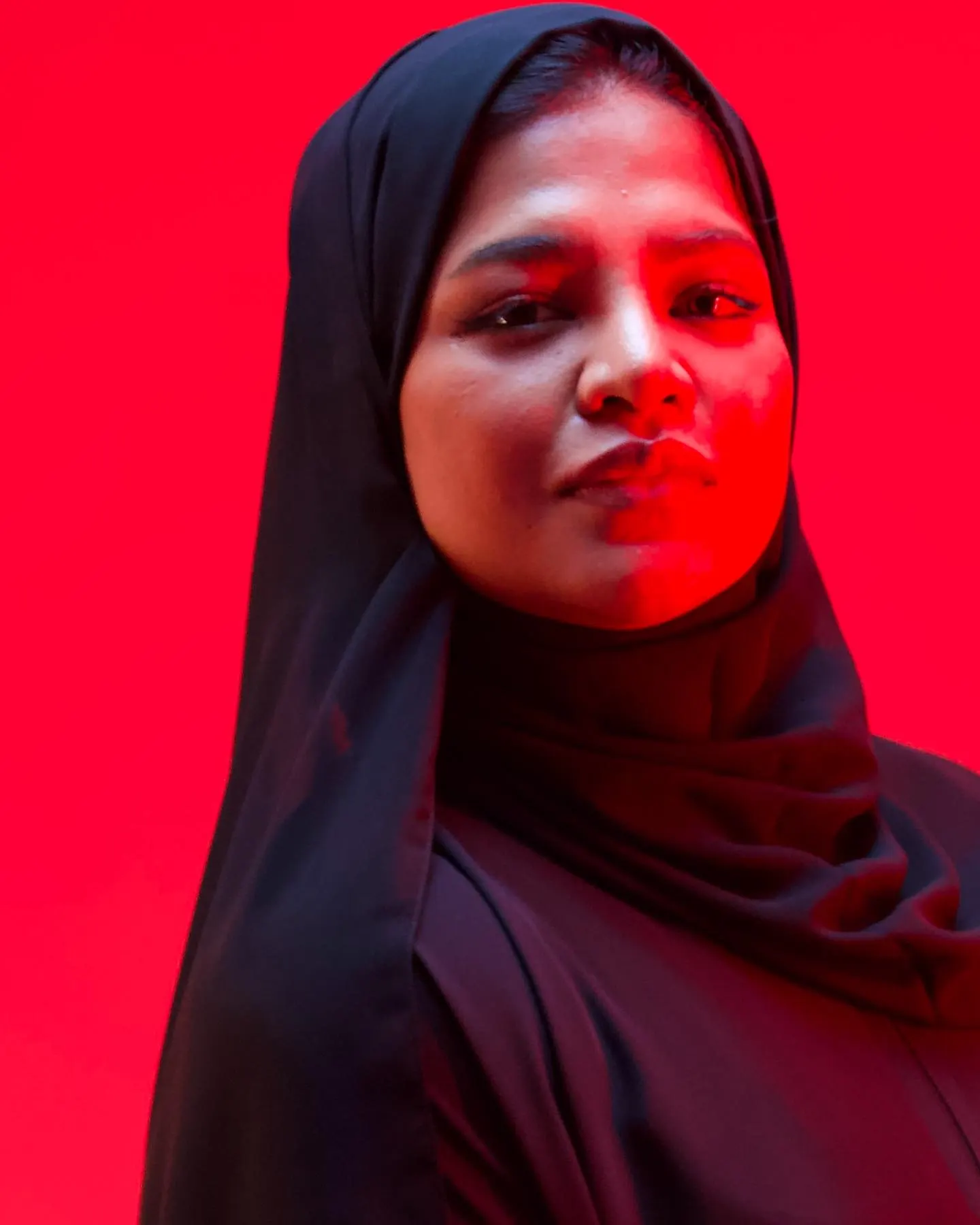 A studio portrait under magenta light of a woman in a black hijab facing the camera
