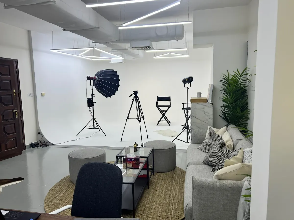 White cyclorama studio with lighting stands, a tripod and a lounge seating area
